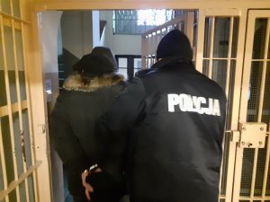 umundurowany policjant służby konwojowej wyprowadza z pomieszczenia dla osób zatrzymanych mężczyznę