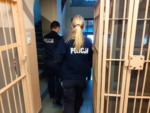 umundurowani policjant i policjantka wyprowadzają z okratowanego korytarza pomieszczenia dla osób zatrzymanych skazaną