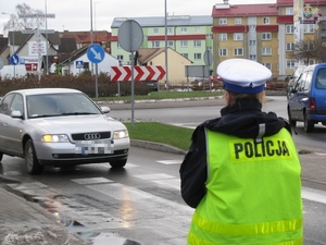 policjantka ruchu drogowego obserwuje skrzyżowanie o ruchu okrężnym. Ze krzyżowania zjeżdża samochód osobowy