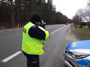 przy zaparkowanym na poboczu drogi k6 radiowozie stoi skierowany tyłem do obiektywu policjant ruchu drogowego, który mierzy prędkość ręcznym miernikiem