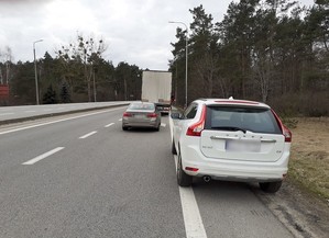 na poboczu stoi białe osobowe volvo, przed nim znajduje się nieoznakowany radiowóz. Przed radiowozem stoi pojazd ciężarowy