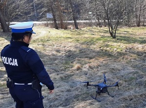 policjantka ruchu drogowego stoi przed znajdującym się na polnej drodze dronem