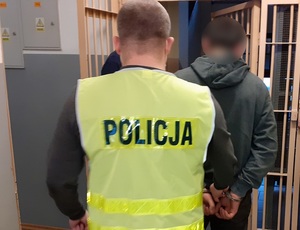 policjant wyprowadza z korytarza pomieszczenia dla osób zatrzymanych mężczyznę