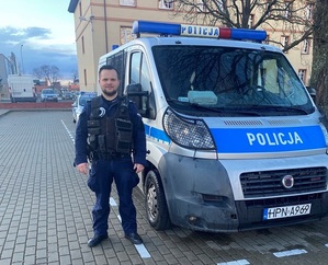 obok oznakowanego radiowozu stoi policjant służby prewencyjnej