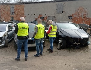 przed częściowo zdemontowanymi samochodami stoją od lewej funkcjonariusz KAS, policjant, inspektor WIOŚ