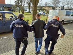 dwaj policjanci prowadzą w kierunku radiowozu zatrzymanego mężczyznę