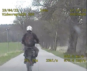 kadr z nagrania wideorejestratora policyjnego radiowozu przedstawiającego jadącego środkiem drogi motocyklistę