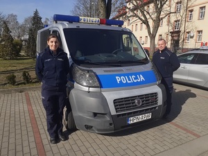 po obu stronach oznakowanego radiowozu stoją umundurowani policjant i policjantka