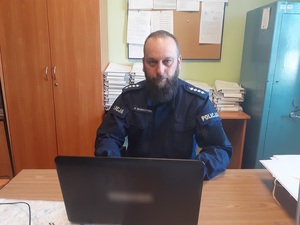 przy biurku przed laptopem siedzi umundurowany policjant