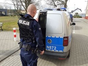 przy uchylonych tylnych drzwiach oznakowanego radiowozu stoi policjant służby patrolowej