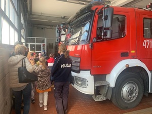 w pomieszczeniu straży pożarnej obok wozu strażackiego stoi umundurowana policjantka w gronie pierwszaków