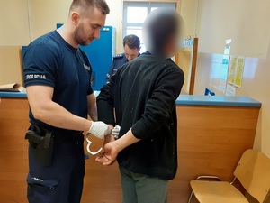 w pomieszczeniu depozytowym komendy policji policjant zakłada kajdanki mężczyźnie