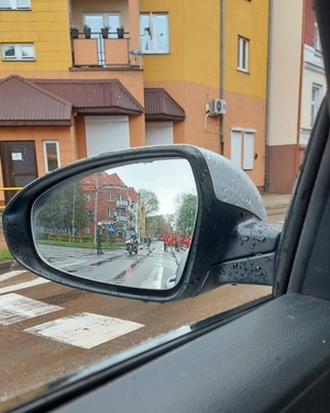 w bocznym lusterku samochodowym odbijają się uczestnicy przemarszu oraz policjant kierujący ruchem