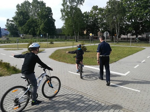 policjant ruchu drogowego przeprowadza na terenie policyjnego miasteczka ruchu drogowego egzamin praktyczny z jazdy rowerem
