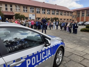 na placu przed szkołą policjant ruchu drogowego prowadzi rozmowę ze zgromadzonymi uczniami