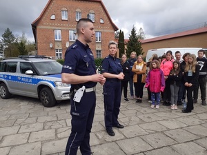 na szkolnym placu na tle dwóch oznakowanych radiowozów policjantka i policjant ruchu drogowego prowadzą rozmowę z uczniami