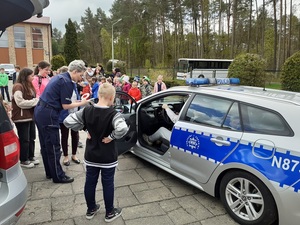 dzieci oglądają radiowóz, niektóre siedzą w środku auta. Rozmawia z nimi policjantka, pochylona nad otwartymi drzwiami auta