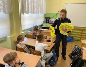 policjantka rozdaje siedzących w szkolnych ławkach dzieciom kamizelki odblaskowe