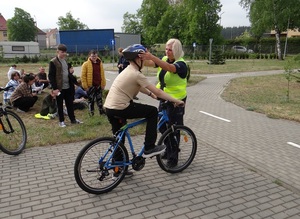 na terenie miasteczka ruchu drogowego lęborskiej komendy Policji policjantka ruchu drogowego poprawia kask ochronny na głowie siedzącego na rowerze chłopca