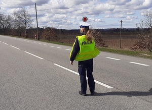 na jezdni stoi policjantka ruchu drogowego z uniesioną do góry tarczą do zatrzymywania pojazdów