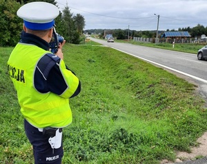 policjant ruchu drogowego stoi przy drodze i mierzy prędkość przejeżdżających pojazdów za pomocą ręcznego miernika prędkości