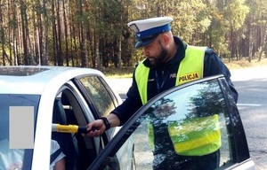 policjant ruchu drogowego poddaje siedzącą w samochodzie na miejscu kierowcy osobę badaniu alkotestem