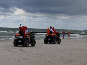 wzdłuż linii brzegowej na plaży dwoma quadami jadą mieszane patrole składające się z ratownika wodnego i policjanta