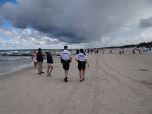 plażą wzdłuż linii brzegowej idzie policyjny patrol