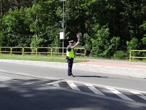 na środku jezdni stoi policjant ruchu drogowego nadający tarczą do zatrzymywania pojazdów sygnał