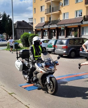 ulicą jedzie policjant na motocyklu. Przed nim i za nim znajdują się biegacze