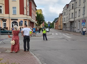 na skrzyżowaniu stoi policjant ruchu drogowego. Na chodnikach znajdują się obserwatorzy biegu ulicznego