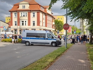 wjazd na skrzyżowanie blokuje policyjny radiowóz. Na skrzyżowaniu stoi policjant ruchu drogowego. Wzdłuż trasy biegu stoją obserwatorzy. Ulicą biegną zawodnicy