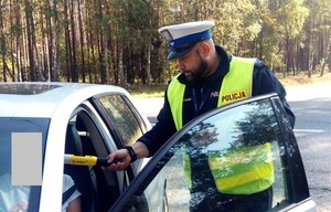 policjant ruchu drogowego poddaje badaniu alkotestem osobę siedzącą za kierownicą samochodu