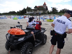 na plaży policjantka siedzi na quadzie i przygotowuje się do wyjazdu. Obok stoi policjant