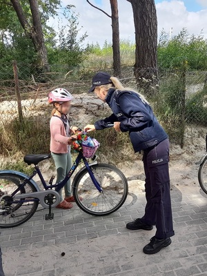 przed wejściem na plażę policjantka wkłada do koszyka rowerowego dziewczynki ulotkę