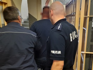 dwaj policjanci wyprowadzają zatrzymanego mężczyznę z zakratowanego pomieszczenia