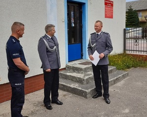 przed wejściem do komisariatu policji stoi Komendant Powiatowy Policji w Lęborku oraz nowo powołany Komendant Komisariatu, który trzyma w dłoniach teczkę z rozkazem personalnym. Obok Komendanta Powiatowego stoi Kierownik Referatu Prewencji KP w Łebie