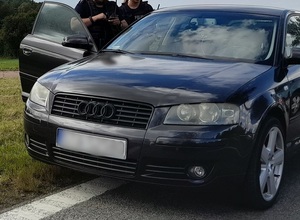 dwoje umundurowanych policjantów stoi przed otwartymi drzwiami od strony pasażera osobowego audi, stojącego na poboczu