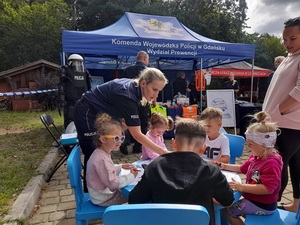 przed stoiskiem profilaktycznym KWP w Gdańsku policjantka nachyla się w kierunku dzieci siedzących przy stoliku