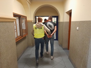 policjant prowadzi korytarzem skutego kajdankami mężczyznę