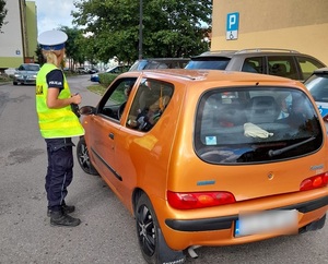 na parkingu przy pomarańczowym seicento stoi policjantka ruchu drogowego