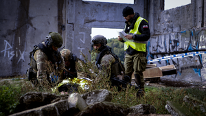 na tle gruzowiska trzech policyjnych kontrterrorystów klęczy przy poszkodowanym okrytym kocem termicznym. Obok nich stoi policjant w odblaskowej kamizelce