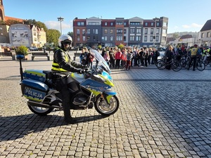 przed zgromadzoną na placu grupą dzieci znajduje się policjant ruchu drogowego na motocyklu