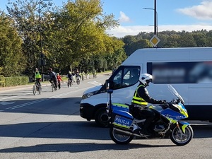 policjant na motocyklu pilotuje przejeżdżającą ulicą grupę rowerzystów