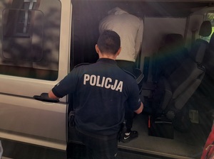 policjant służby konwojowej wprowadza do nieoznakowanego radiowozu zatrzymanego mężczyznę