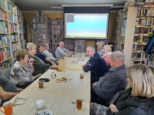 w bibliotece przy stole siedzą uczestnicy debaty, w tym umundurowany policjant, który przemawia do zebranych