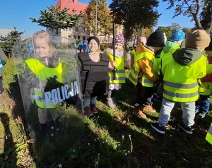 mała dziewczynka trzyma tarczę z napisem policja, stojący obok niej chłopiec ma założoną kamizelkę policyjną, a kolejna dziewczynka trzyma pałkę policyjną