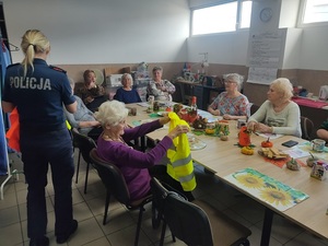 policjantka rozdaje siedzącym przy stole seniorkom kamizelki odblaskowe