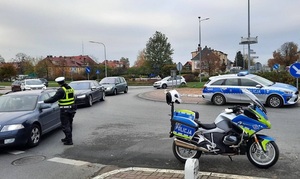 na rondzie stoi policyjny radiowóz i motocykl. Policjant ruchu drogowego kieruje ruchem pojazdów