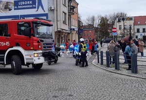 przemarsz uczestników obchodu Narodowego Święta Niepodległości. Przed uczestnikami stoi przy motocyklu policjant. Obok znajduje się wóz straży pożarnej